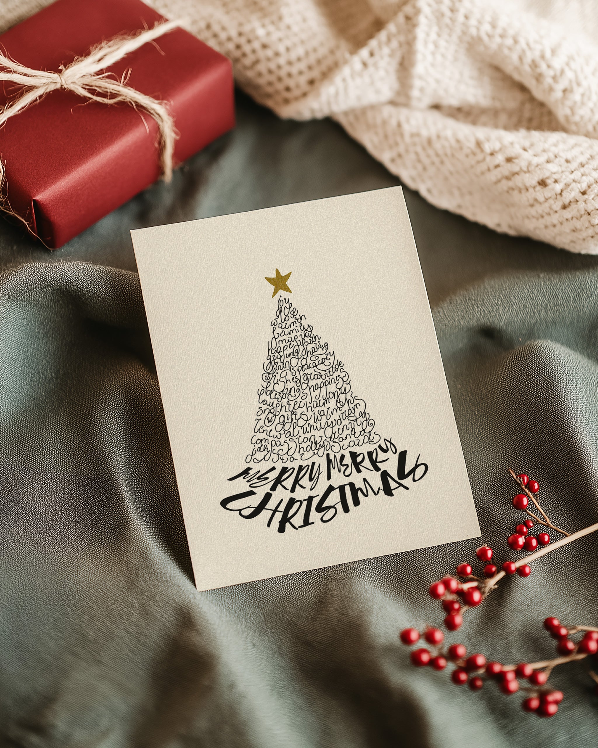 Modern Merry Christmas greeting card with a tree design and 'Merry Christmas' text, surrounded by festive decorations on a wooden surface.