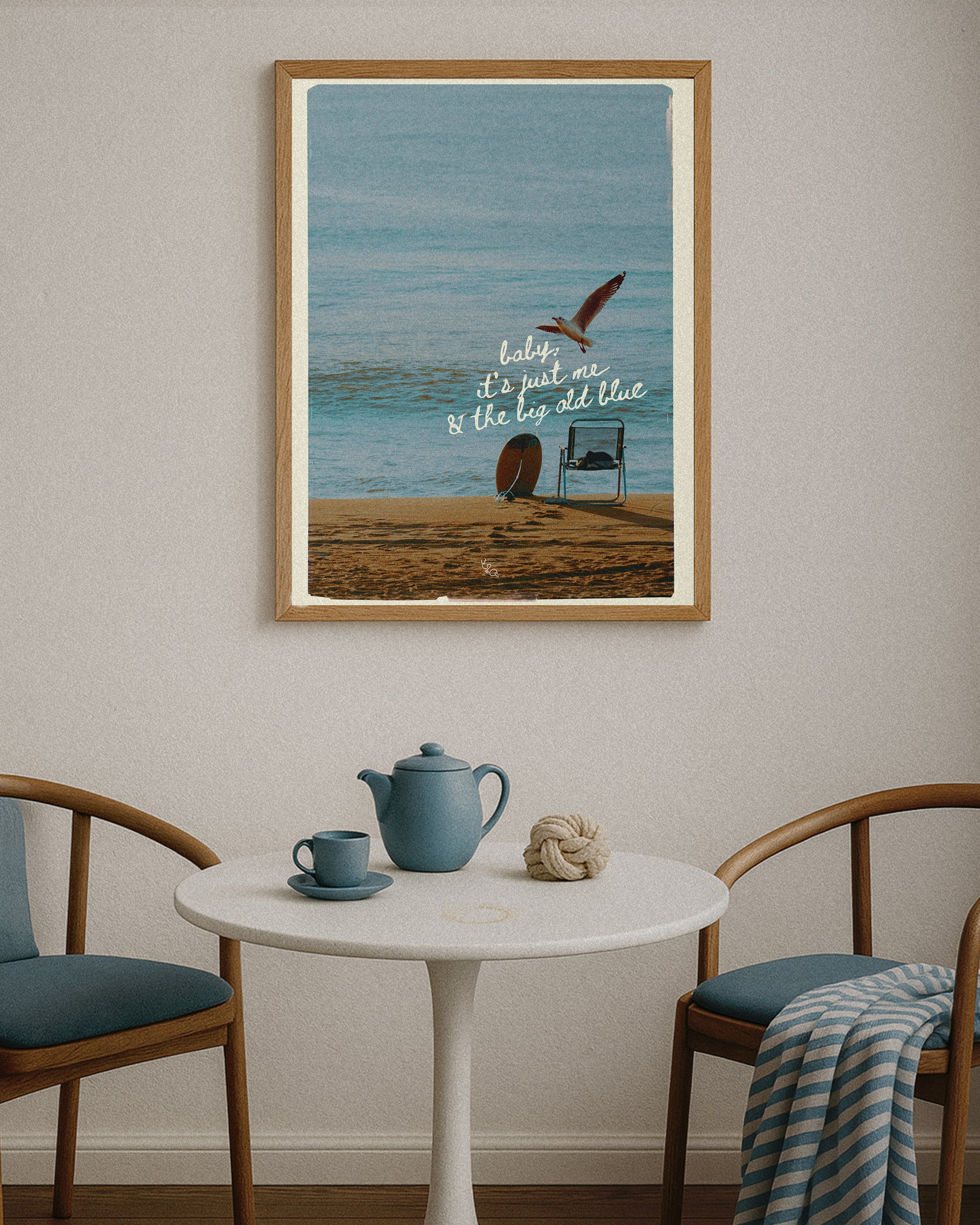 Framed minimalist coastal decor of a beach scene with a quote above a table with a teapot and cup.