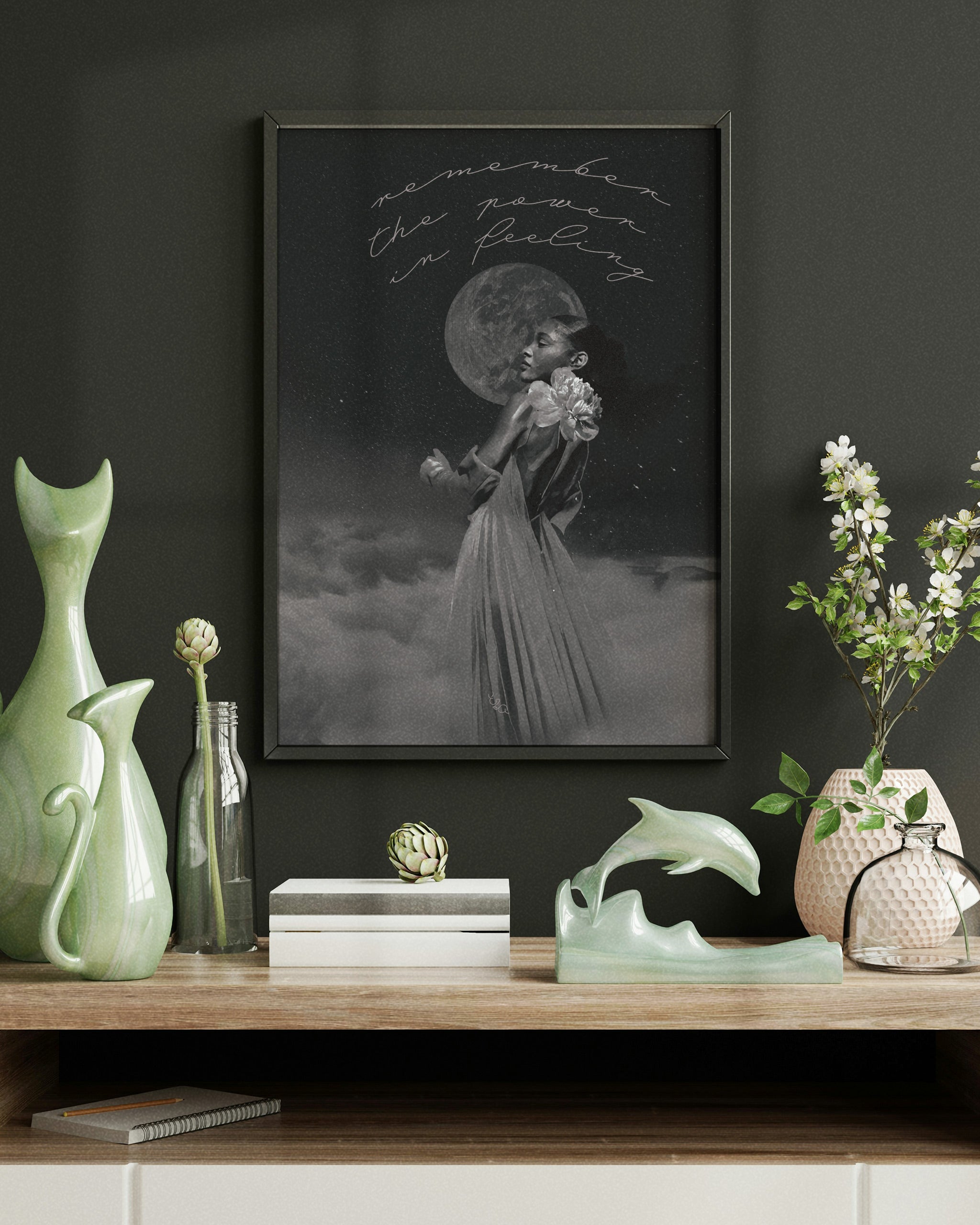 Framed female energy dreamscapes art on a dark wall with decorative items on a wooden shelf.