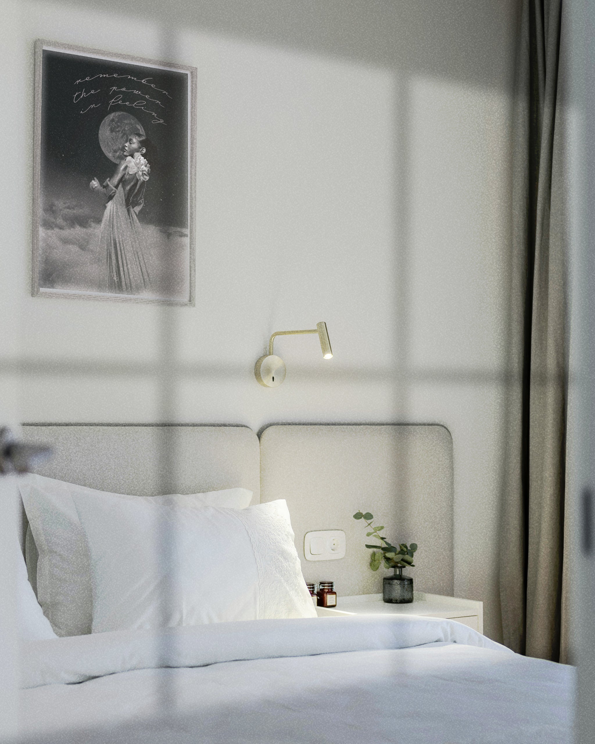 Neatly made bed in a bedroom with a wall lamp and framed The Gentle Empath dreamscape art