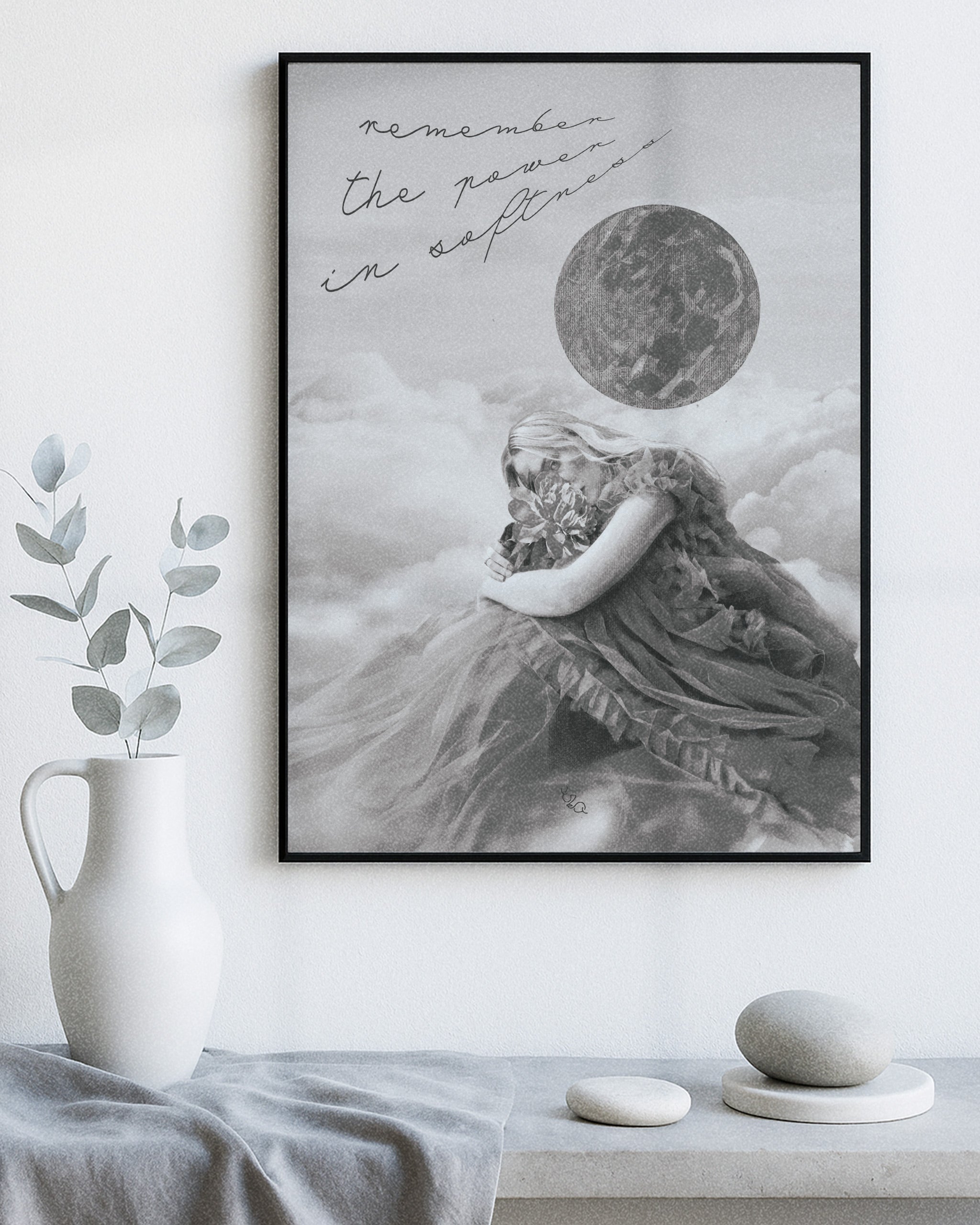Framed female energy modern decorative wall art of a woman embracing a flower with the moon and clouds above her with text "remember the power in softness", placed on a shelf with decorative items.
