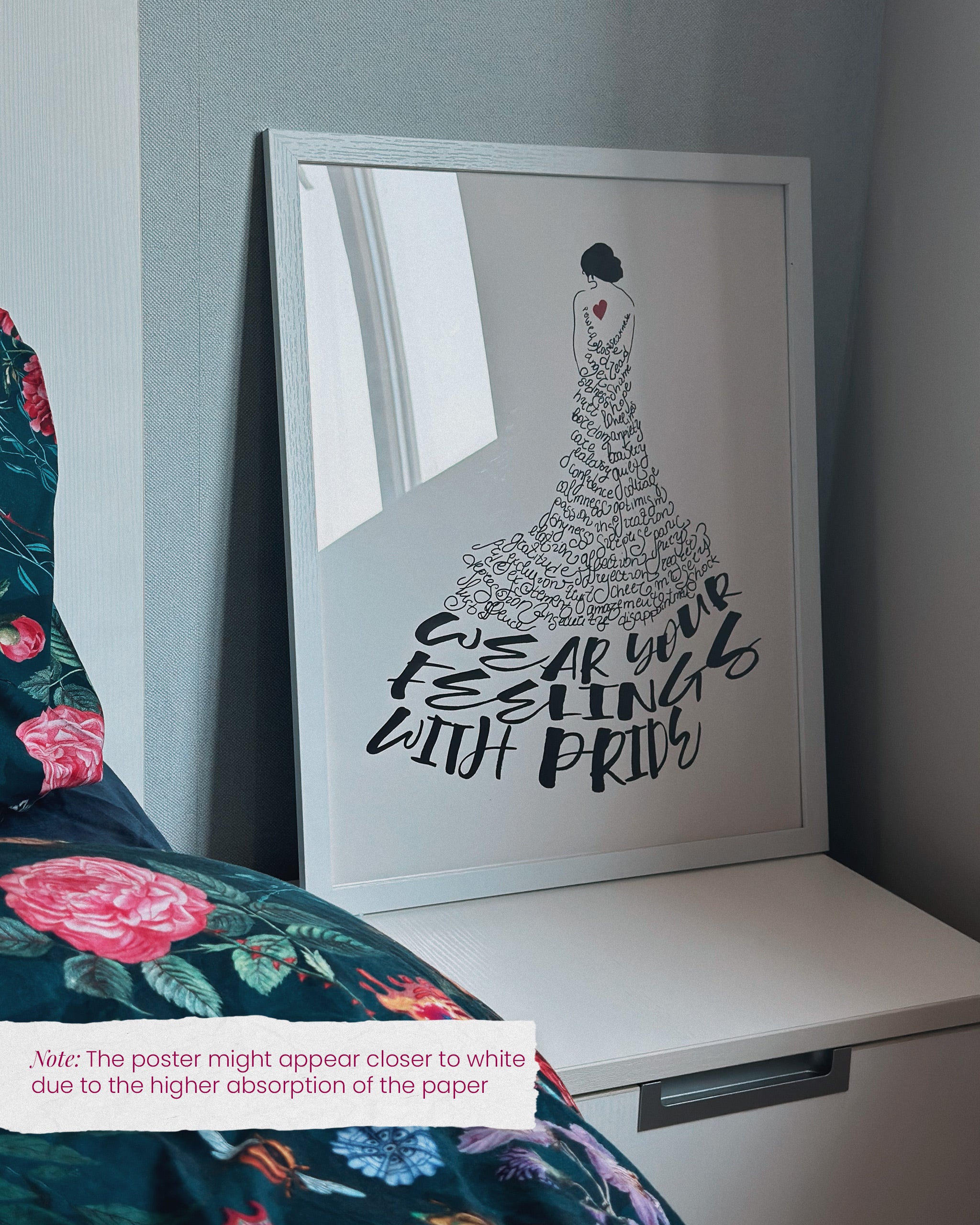 the dress to express self love poster framed in a white frame and shown by a bed with the note that the poster will appear closer to white when less textured paper is used (common for bigger sizes)