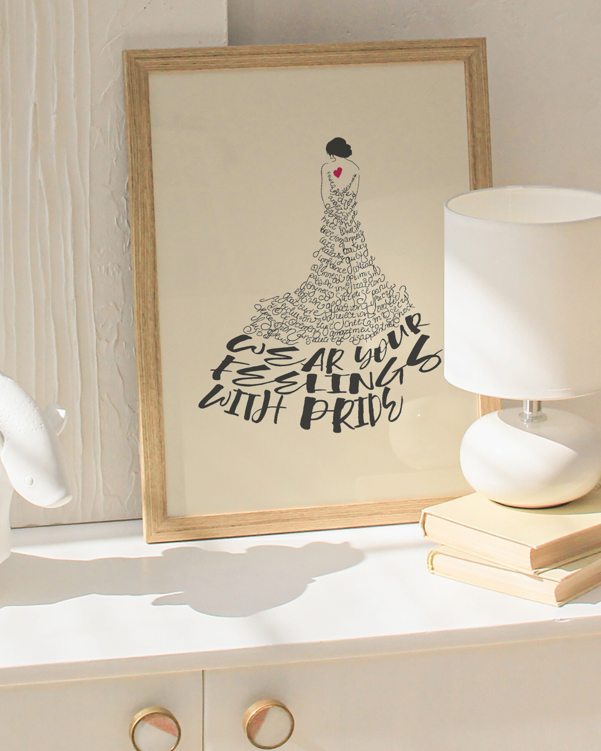 Framed artwork with a stylized dress and text on a shelf with a lamp and books.