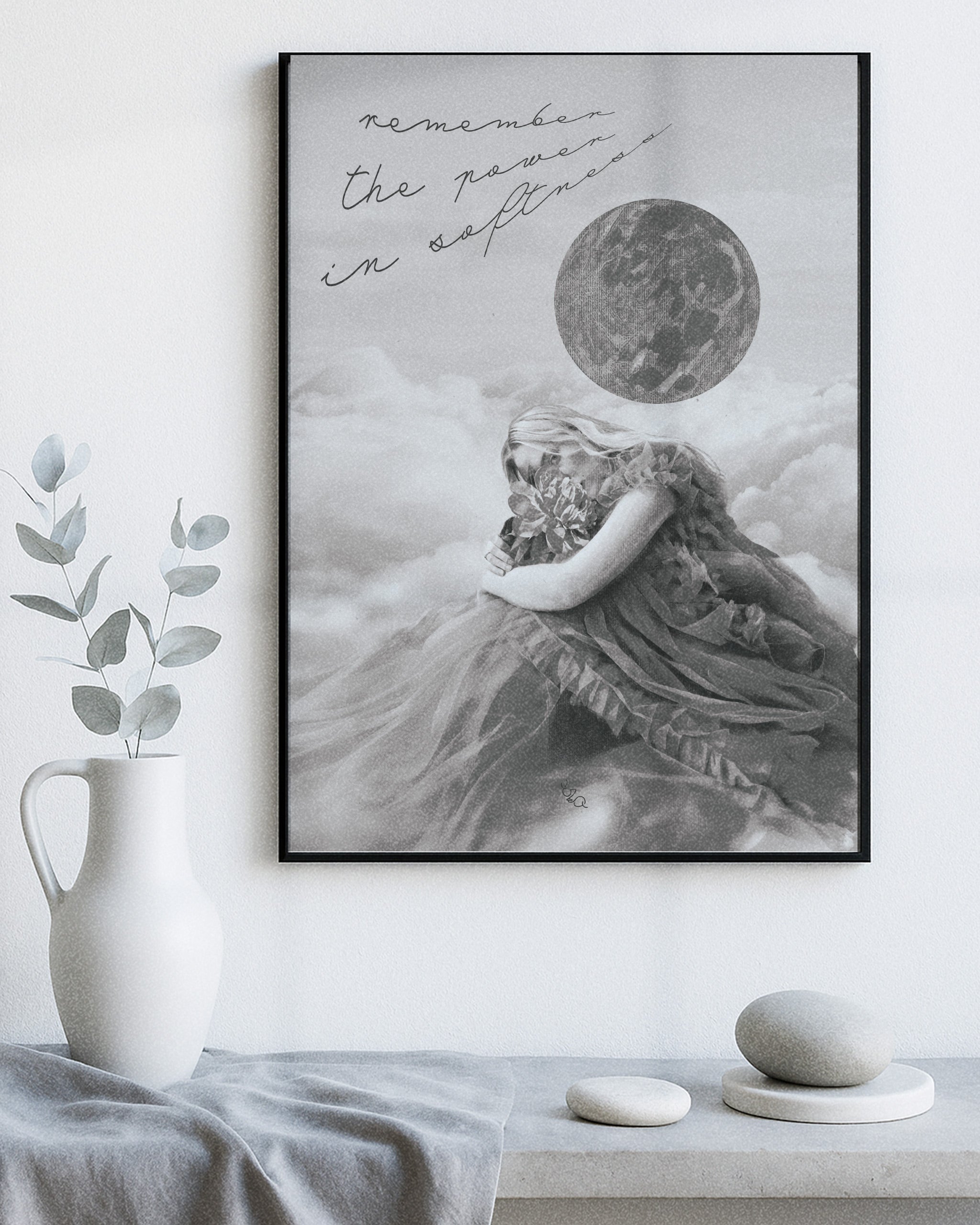 Framed female energy modern decorative wall art of a woman embracing a flower with the moon and clouds above her with text "remember the power in softness", placed on a shelf with decorative items.