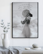 Framed modern decorative artwork of a woman in a dress with a moon in the sky, placed on a white wall above a table with decorative items.