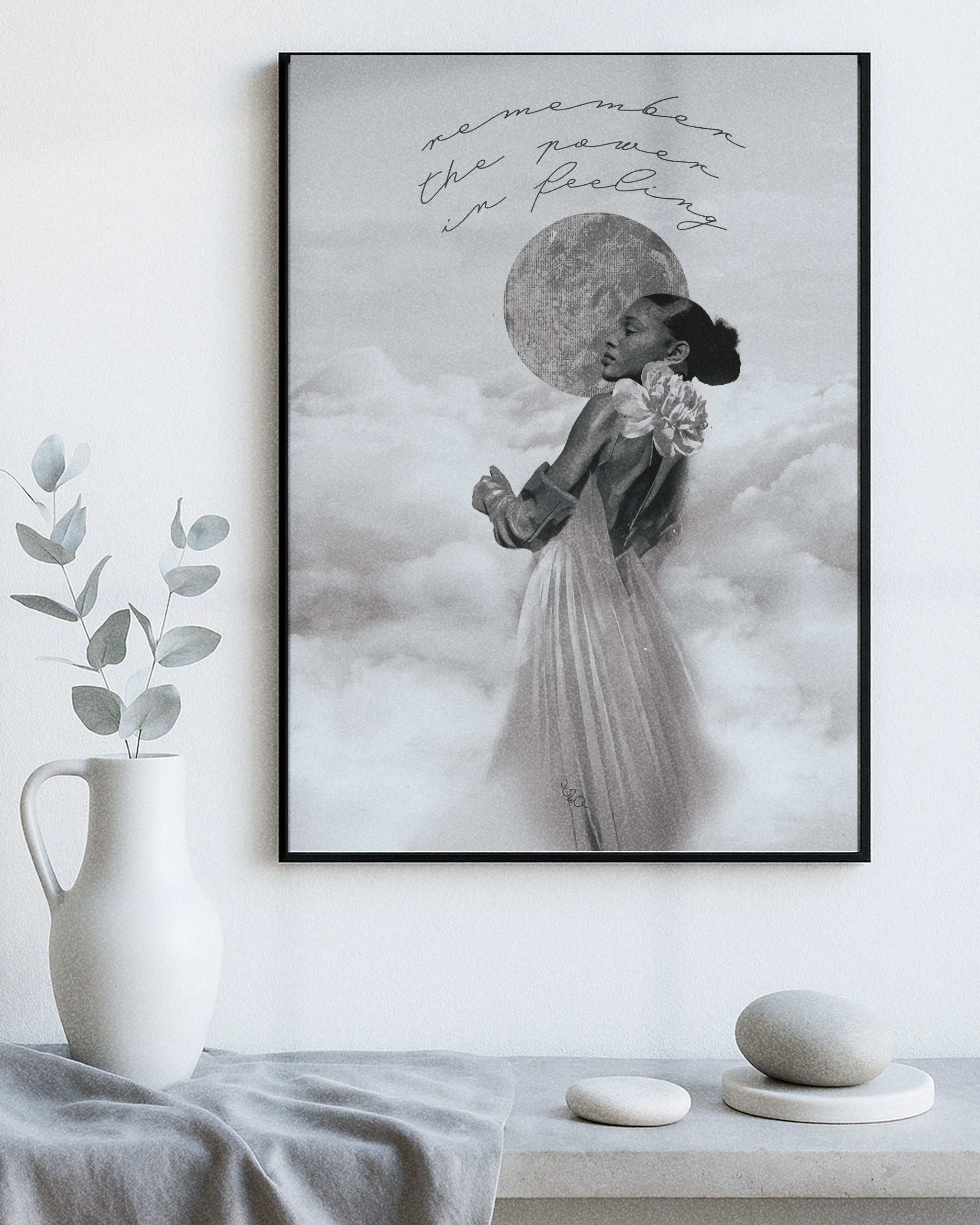 Framed modern decorative artwork of a woman in a dress with a moon in the sky, placed on a white wall above a table with decorative items.