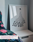 the dress to express self love poster framed in a white frame and shown by a bed with the note that the poster will appear closer to white when less textured paper is used (common for bigger sizes)